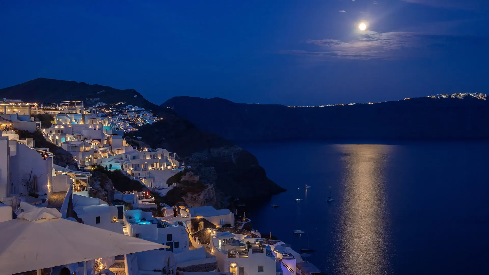 Oia village on the Santorini caldera at night, white-washed buildings and moonlight over the Aegean Sea